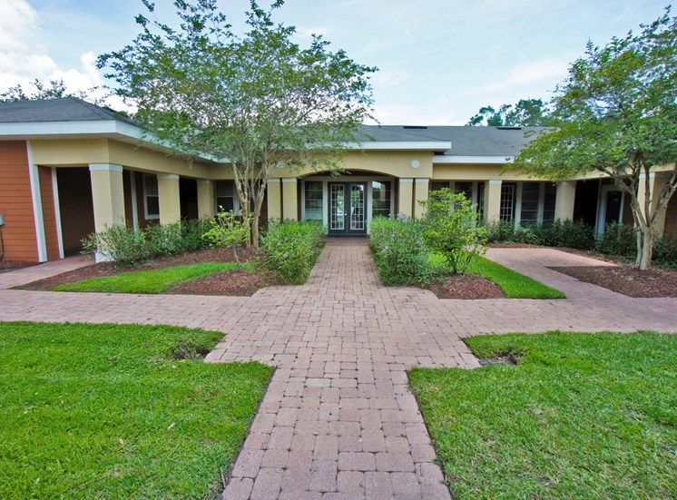 Clubhouse exterior with pavers leading to the office with bushes and trees in front of them